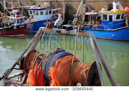 WHITSTABLE, UK - OCTOBER 15, 2017: Close-up on a seagull and a capstan at the fishing Harbor with fishing boats in the background