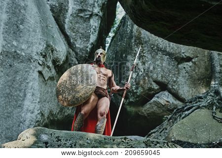 Full length low angle shot of a Spartan warrior with sexy muscular strong body posing on top of a rock armored looking away copyspace.