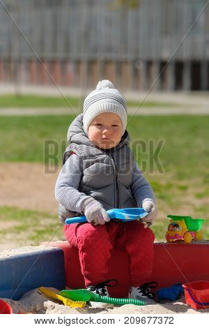 Portrait of toddler child wearing vest jacket outdoors. One year old baby boy playing with sand at playground sandbox