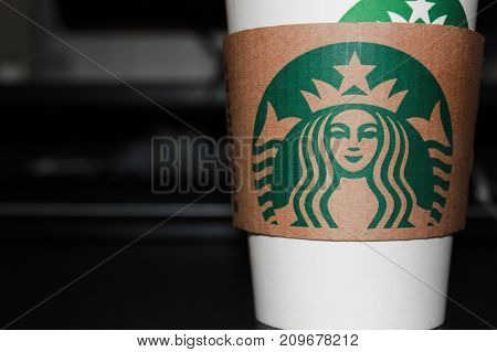 MOSCOW, RUSSIA - OCTOBER 9, 2017: Starbucks Coffee To Go paper Cup on Black Table at the Office Background. Take away drink in white cup with Starbucks logo in front of the computer at workplace.