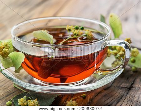 Cup of linden tea and lime flowers on the wooden table.