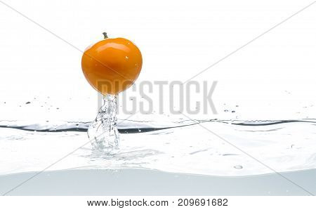 Whole, yellow and ripe tomato falls into the water. Water splashes. Isolated picture on white background