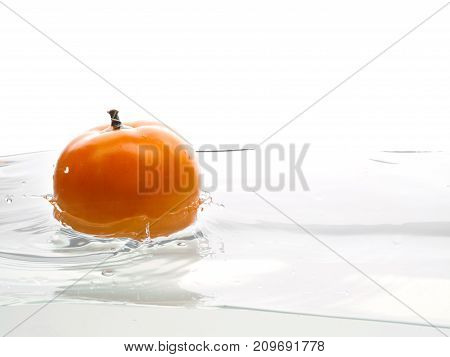 Whole, yellow and ripe tomato falls into the water. Water splashes. Isolated picture on white background