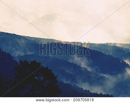 Distant Mountain Range And Heavy Clouds Of Colorful  Mist Above Deep Valleys