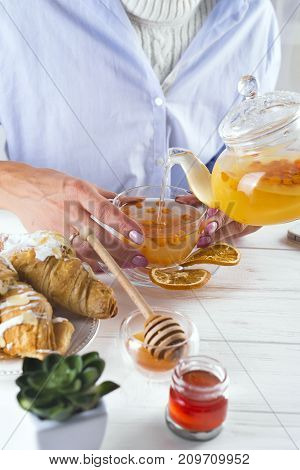 famele hands holding hot cup of sea-buckthorn tea.breakfast with croissants and honey