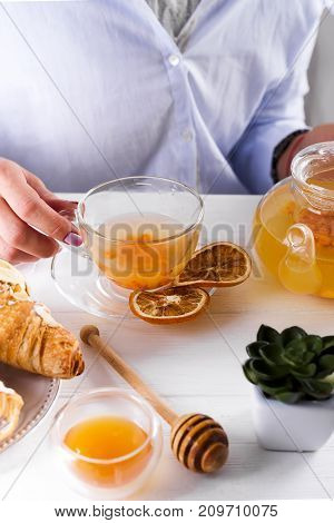 famele hands holding hot cup of sea-buckthorn tea.breakfast with croissants and honey