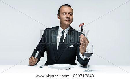 Portrait of a young man in image of maniak with knife, fork and and a piece of raw meat on a plate. Man in suit. The image in the style of Halloween