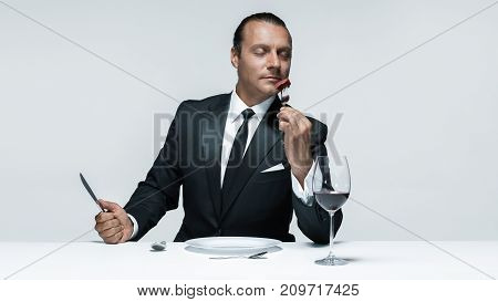 Portrait of a young man in image of maniak with knife, fork and and a piece of raw meat on a plate. Man in suit. The image in the style of Halloween