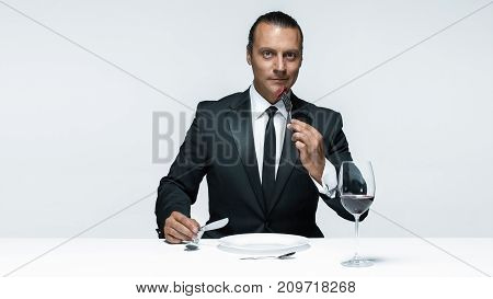 Portrait of a young man in image of maniak with knife, fork and and a piece of raw meat on a plate. Man in suit. The image in the style of Halloween