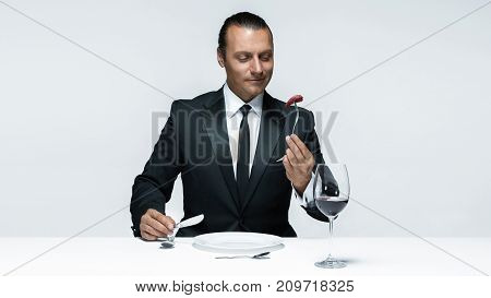 Portrait of a young man in image of maniak with knife, fork and and a piece of raw meat on a plate. Man in suit. The image in the style of Halloween