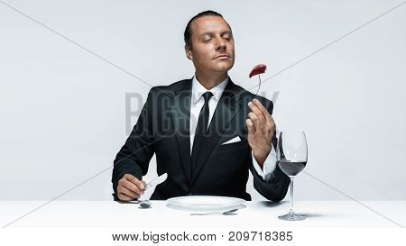Portrait of a young man in image of maniak with knife, fork and and a piece of raw meat on a plate. Man in suit. The image in the style of Halloween