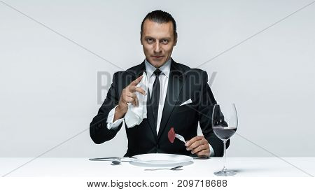 Portrait of a young man in image of maniak with knife, fork and and a piece of raw meat on a plate. Man in suit. The image in the style of Halloween