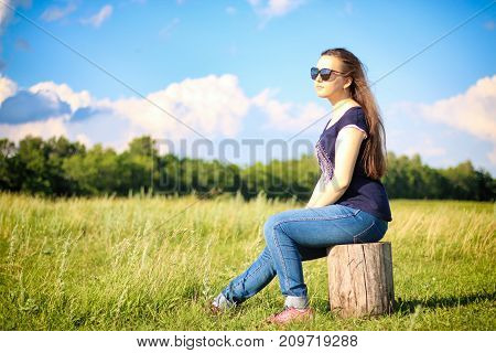 Girl sitting on a tree stump in the field.