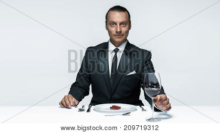 Portrait of a young man in image of maniak with knife, fork and and a piece of raw meat on a plate. Man in suit. The image in the style of Halloween