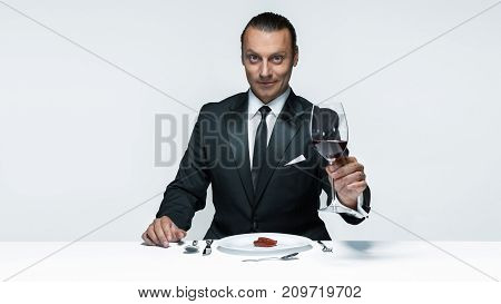 Portrait of a young man in image of maniak with knife, fork and and a piece of raw meat on a plate. Man in suit. The image in the style of Halloween