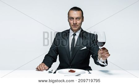 Portrait of a young man in image of maniak with knife, fork and and a piece of raw meat on a plate. Man in suit. The image in the style of Halloween