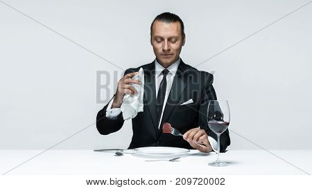 Portrait of a young man in image of maniak with knife, fork and and a piece of raw meat on a plate. Man in suit. The image in the style of Halloween