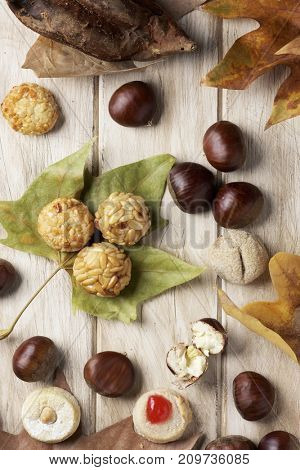 high-angle shot of a roasted sweet potato, some chestnuts and some panellets, as a typical snack eaten in All Saints Day in Catalonia, Spain, called castanada, and some autumn leaves on a wooden table