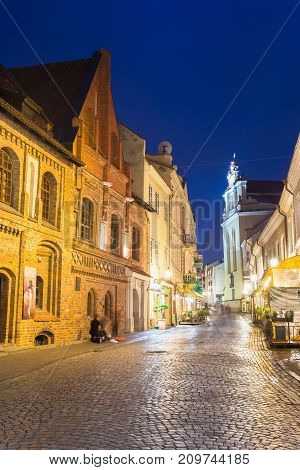 Vilnius, Lithuania - July 8, 2016: Illuminated Facades Of Ancient Buildings On Famous Pilies Street Of Old Town In Night, Popular Showplace Under Summer Dark Blue Sky.