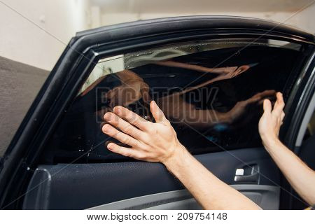 Master installs a tint film for the car glass with a hairdryer and spatula with glare of light. Concept tinting car