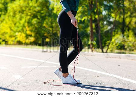 legs of sport girl that doing exercises with jumping rope. White sneakers, black leggings and sexy legs