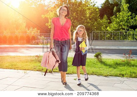 Mom and schoolgirl of primary school holding hands. The parent takes the child to school. Outdoors return to the concept of the school