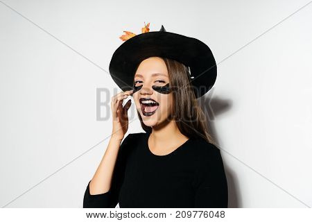 a young sexy gothic girl dressed in a witch for a halloween, in a big black hat and laughs