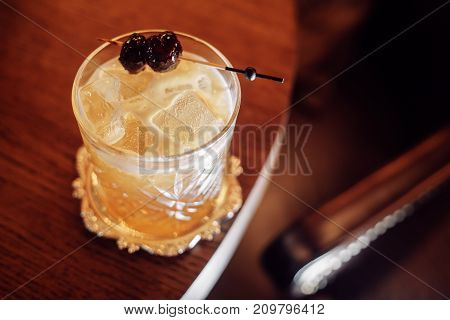 rich yellow cocktail with ice and cherry on a stick over lucksherry background