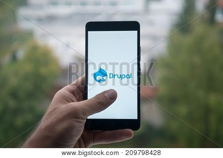 London, United Kingdom, october 3, 2017: Man holding smartphone with Drupal logo with the finger on the screen