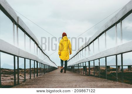 Woman walking away on bridge road Travel Lifestyle emotional concept vacations outdoor yellow raincoat clothing