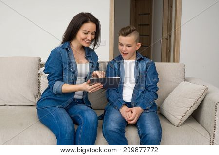 Happy mother and son sitting on sofa and using digital tablet at home