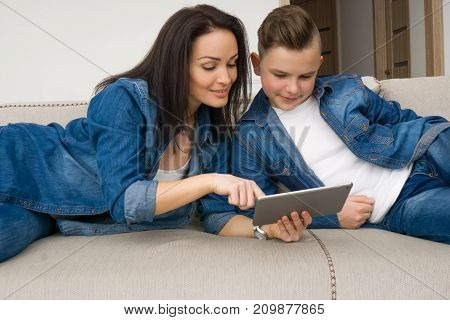 Happy mother and son sitting on sofa and using digital tablet at home