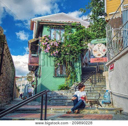ISTANBUL TURKEY: Pretty girl sitting with cat on stair of old street with cute green house in Uskudar district on October 3 2017