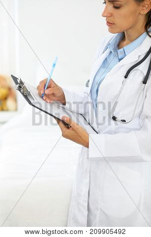 Close-up of a female doctor filling  up medical form at clipboard while standing straight in hospital.
