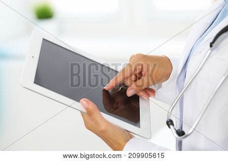 Woman doctor using tablet computer while standing straight in hospital.