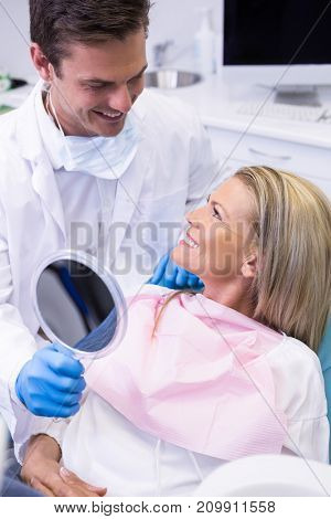 Dentist showing mirror to happy patient at dental clinic
