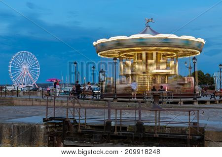HONFLEUR, FRANCE - AUGUST 24, 2017: Caroussel and ferris wheel at the harbor of Honfleur. Long exposure image in the evening with rotating carrousel