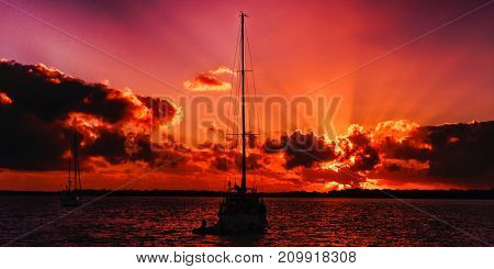 A striking inspirational red coloured cloudy sea water sunrise seascape featuring a sailing yacht in silhouette with ocean water reflections. Fraser Island Queensland Australia.