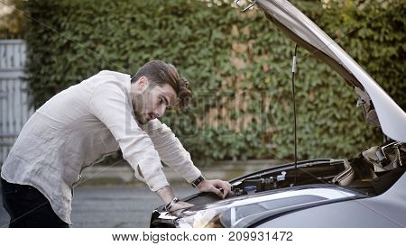 Handsome young man trying to repair a car engine, looking inside open bonnet