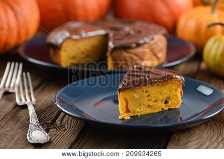 Delicious homemade pumpkin cake with chocolate icing served on dark blue plates with bright orange pumpkins closeup