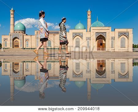 Two Women Stroll In Front Of The Khast-imam Mosque, Reflected In Puddle Of Water