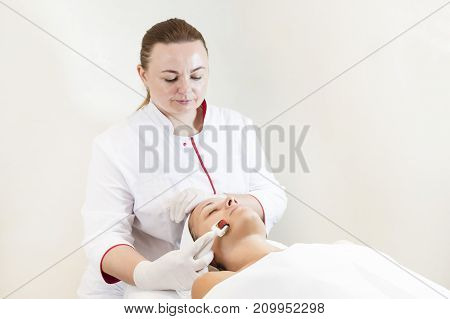 The woman undergoes the procedure of medical micro needle therapy with a modern medical instrument derma roller.