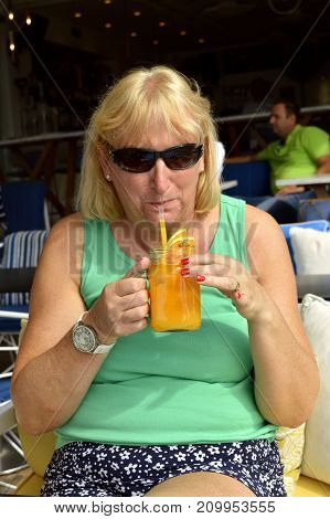 Paxos Corfu Greece - October 1 2017 : Lady drinking a glass of fresh orange in Paxos harbour