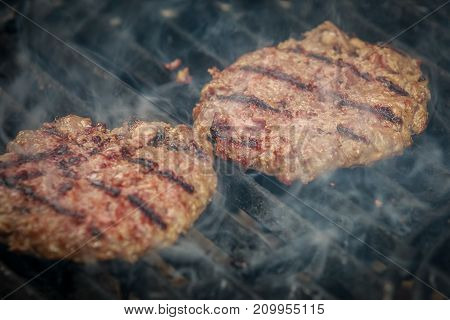 Succulent and appetizing beef hamburgers are roasting on BBQ grill with smoke