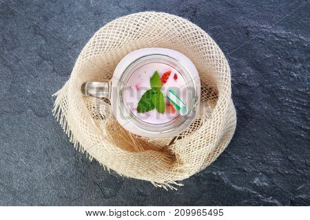 A top view on a mason jar with jogurt and pieces of strawberries and green leaflets of mintson on a marble background. Close-up of drink. Food concept.