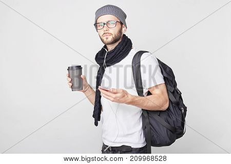 Pensive bearded European hipster guy wearing trendy hat and t-shirt drinks morning coffee listens to sad melodies as being upset missing his girlfriend remembers pleasant moments enjoys his trip.