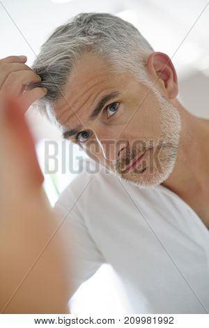 40-year-old man checking hair in front of mirror