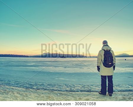 Traveler Stay On Ice Of Frozen Sea. Woman With Backpack And Long Warm Jacket. Footprints In Ice Of L