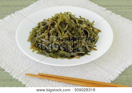 White Plate With Slices Of Pickled Kelp Or Laminaria And Chopsticks On A Fringed Table Napkin. Edibl