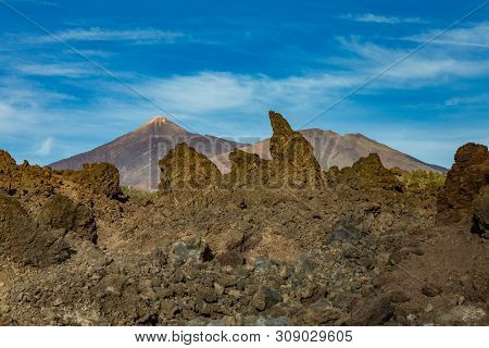 Mountains And Lava Fields Around Volcano Teide, Partly Covered By The Clouds. Bright Blue Sky. Teide